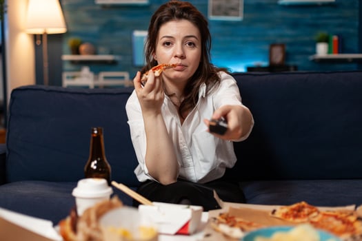 Portrait of caucasian female sitting on sofa eating slice of pizza enjoying takeaway food home delivered in living room. Woman relaxing in living room ordering tasty delicious meal lunch. photo