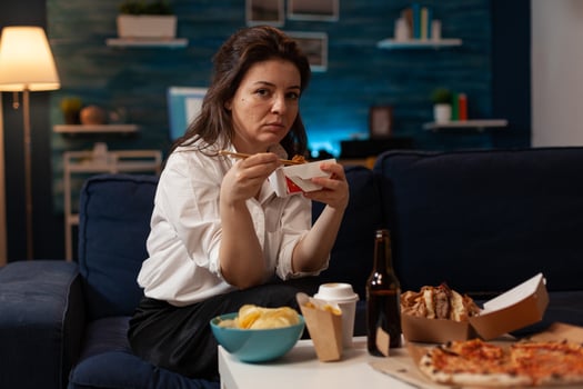 Portrait of smiling woman eating takeout asian noodles with chopsticks on living room sofa. Office worker sitting on couch in the evening enjoying chinese takeaway ramen box and delicious junk food. photo