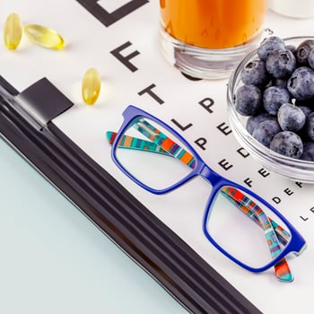 Kid eyeglasses, glass of carrot juice, bowl with natural blueberries photo
