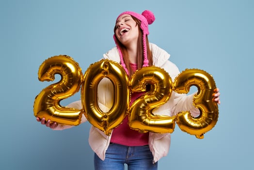 Happy young woman in winter coat holding gold colored numbers against blue background photo