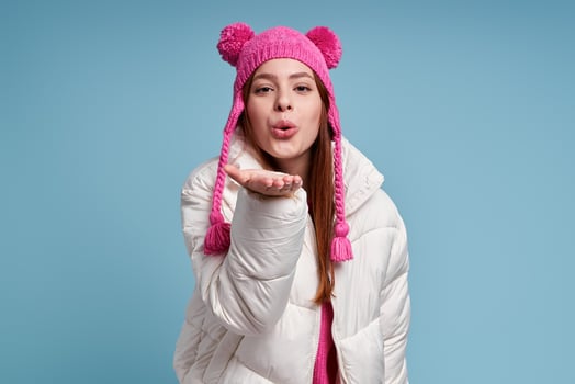 Beautiful young woman in winter coat blowing a kiss while standing against blue background photo