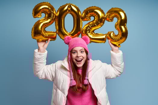 Happy young woman in winter coat holding gold colored numbers against blue background photo