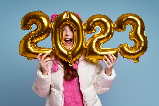 Playful young woman in winter coat holding gold colored numbers against blue background photo