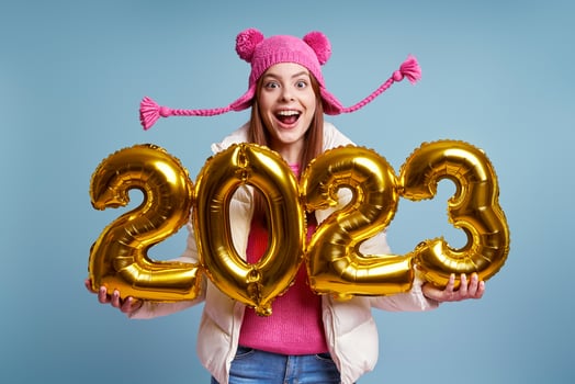 Excited woman in winter coat holding gold colored numbers and smiling against blue background photo