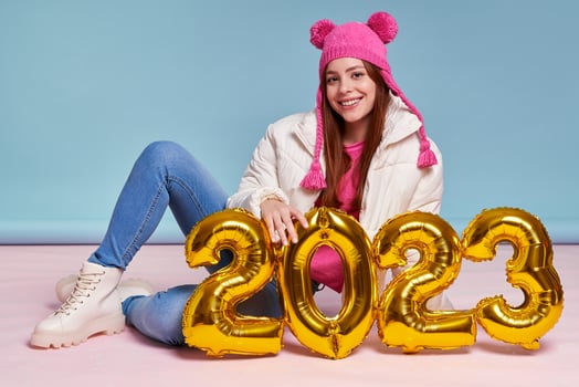 Beautiful young woman in winter coat holding gold colored numbers while sitting against blue background photo