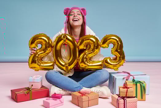 Happy young woman sitting near the gift boxes and gold colored numbers against blue background photo
