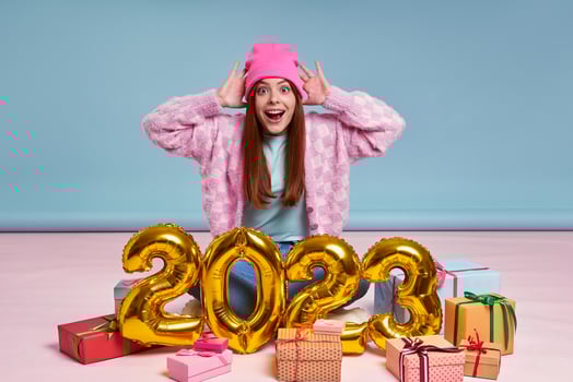 Surprised young woman sitting near the gift boxes and gold colored numbers against blue background photo