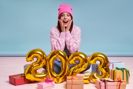 Surprised young woman sitting near the gift boxes and gold colored numbers against blue background photo