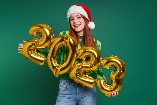 Happy woman in Christmas hat holding gold colored numbers against green background photo