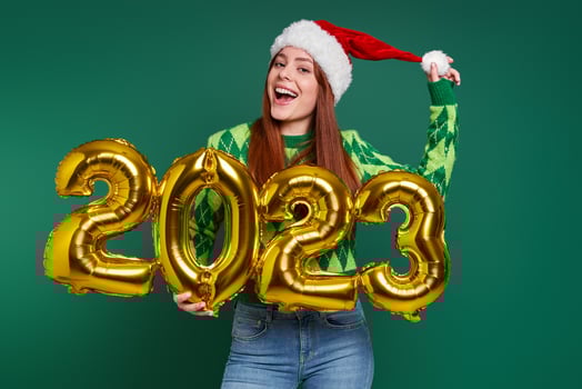 Excited young woman in Christmas hat holding gold colored numbers against green background photo