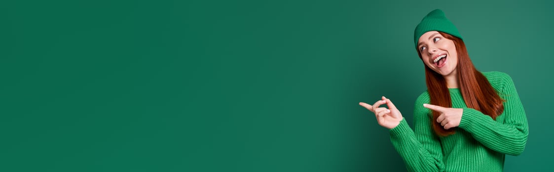 Happy young woman pointing away while standing against green background photo