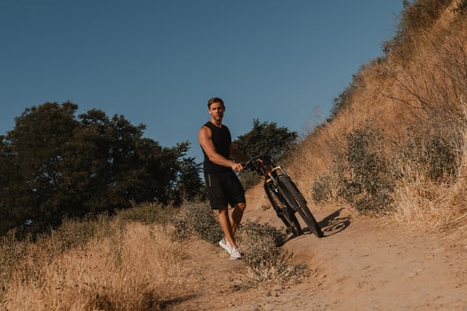 Confident young man in sports clothing pulling his bicycle down by mountain hill photo