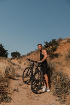 Confident young man in sports clothing pulling bicycle by mountain hill outdoors photo