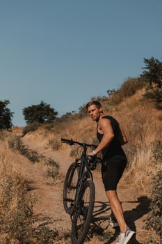Confident young man in sports clothing pulling bicycle by mountain hill outdoors photo