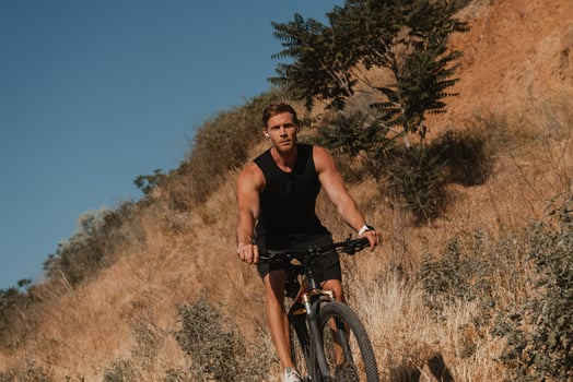 Young athletic man in sports clothing riding bicycle by mountain hill outdoors photo