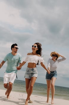 Three beautiful young people looking happy while running by the beach together photo