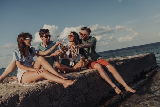 Group of young friends toasting with beer and smiling while spending time seaside together photo