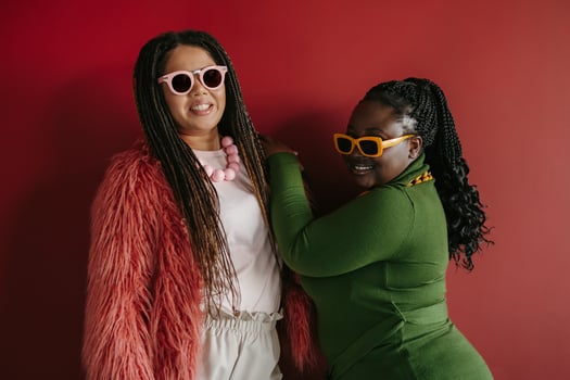 Two fashionable plus size African woman with braided hair smiling while standing on red background together photo