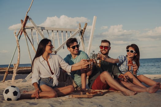 Four happy young people toasting with beer while enjoying pizza on the beach together photo