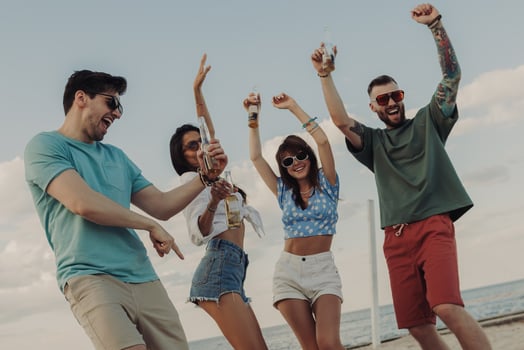 Beautiful young people enjoying cold beer and smiling while dancing on the beach together photo