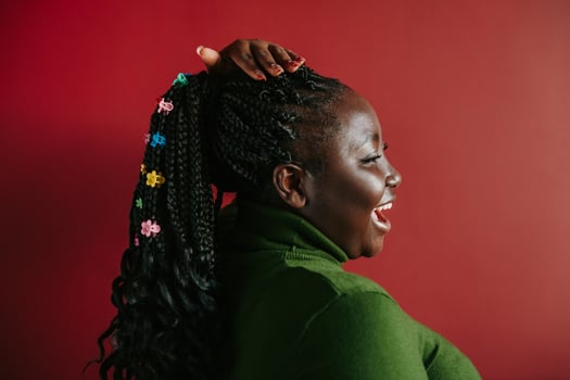 Side view of happy African woman with braided hair and colorful clips standing on red background photo