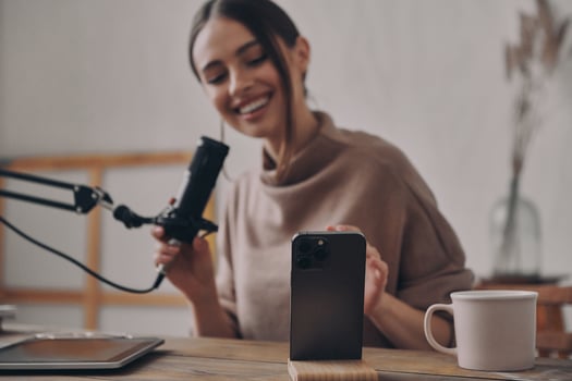 Happy young woman recording podcast while sitting at her workplace in studio photo