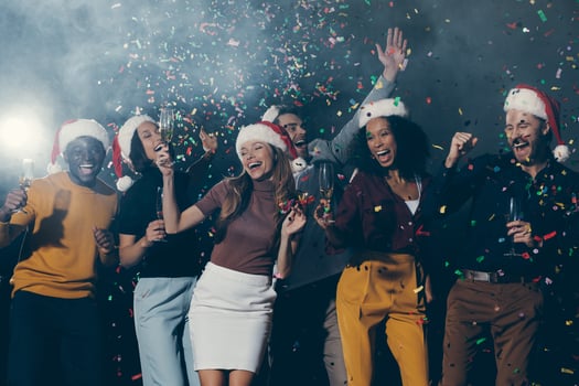 Joyful young people in Christmas hats dancing and throwing confetti while celebrating New Year in night club photo