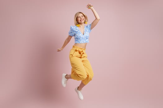 Full length of excited young woman jumping and smiling against pink background photo