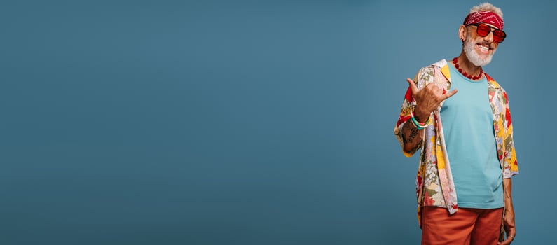 Cool hipster senior man in stylish funky shirt gesturing and smiling against blue background photo