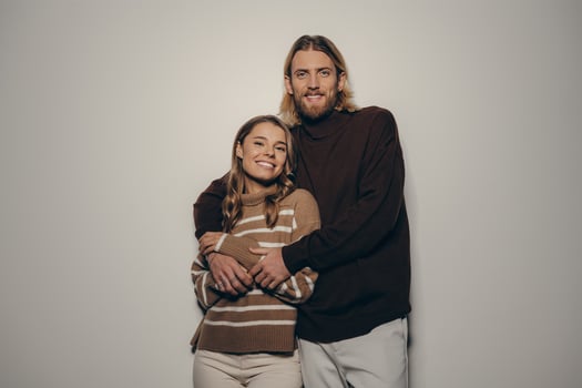 Fashionable young loving couple embracing and looking at camera with smiles on beige background photo