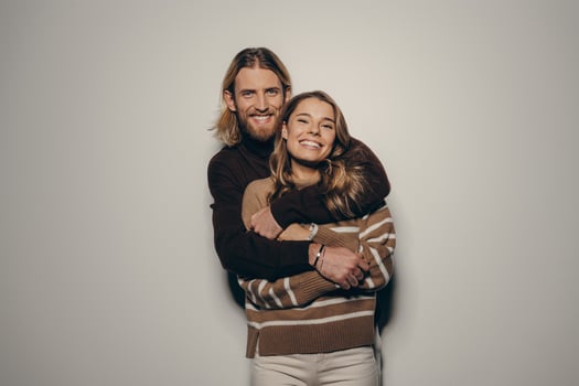 Beautiful young loving couple in cozy warm wear embracing and smiling while standing on beige background photo