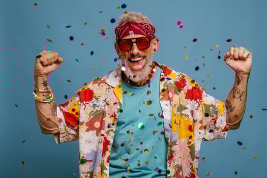 Happy senior man in funky shirt and bandana gesturing while confetti flying around on blue background photo