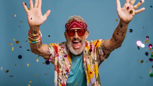 Joyful senior man in funky shirt and bandana throwing colorful confetti on blue background photo