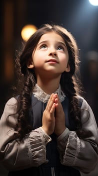 A small 8-year-old white brunette girl folded her hands in a prayerful gesture and looked up photo