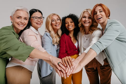 Multi-ethnic group of happy mature women holding hands together against grey background photo