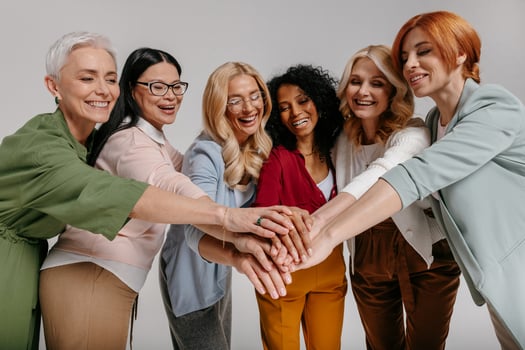 Multi-ethnic group of happy mature women holding hands together against grey background photo