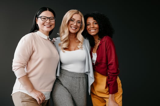 Three happy mature women bonding and smiling against grey background photo