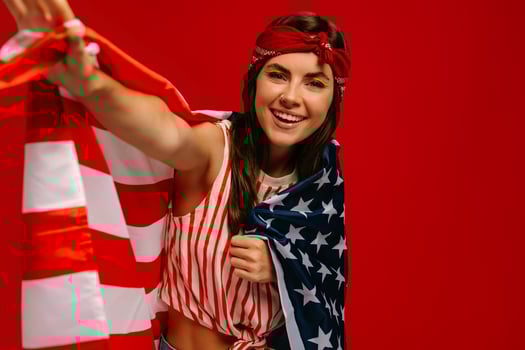Beautiful young hipster woman carrying American flag and smiling while standing on red background photo