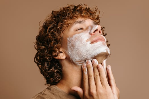 Handsome man enjoying beauty treatment while applying face cream and standing on brown background photo