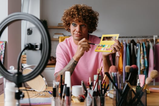 Confident young gay man showing eyeshadow palette while recording make-up tutorial from home photo