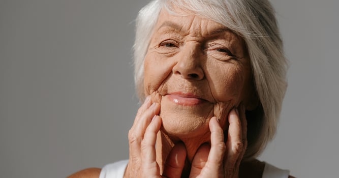 Portrait of beautiful senior woman touching face and smiling against grey background photo