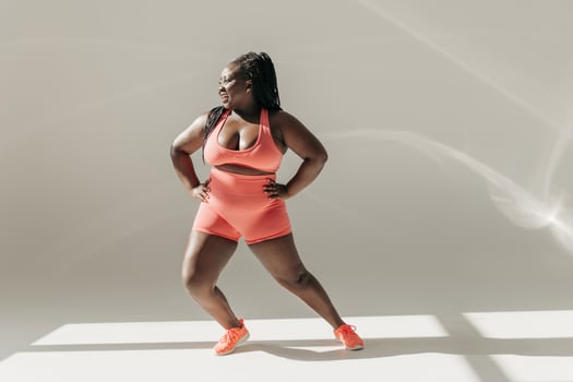 Full length of happy African plus size woman in sportswear warming up before training in fitness studio photo