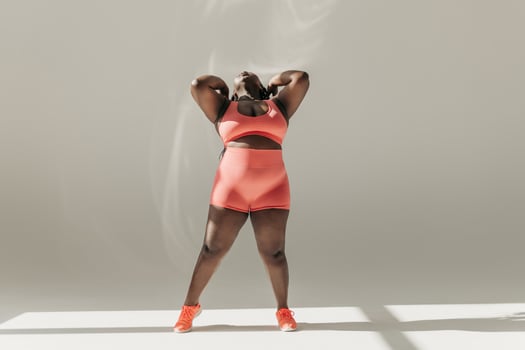 Full length of confident African plus size woman in sportswear adjusting hair while standing in fitness studio photo