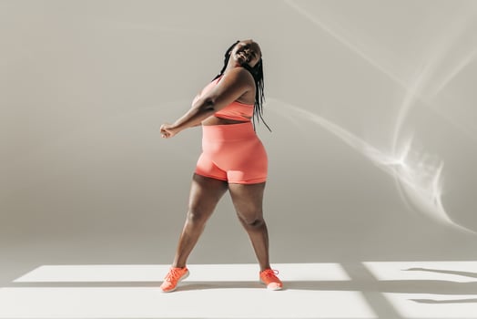 Full length of happy African plus size woman in sportswear doing stretching exercises in fitness studio photo