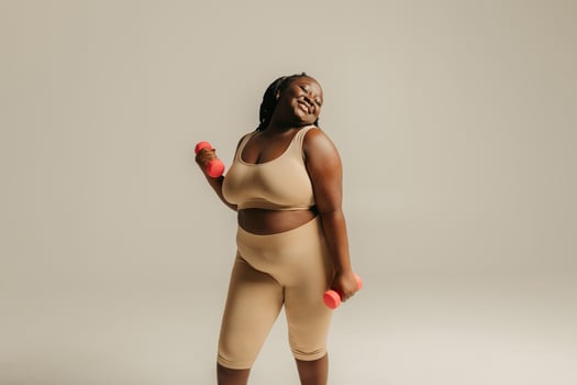Confident plus size African woman in sportswear exercising with dumbbells on studio background photo