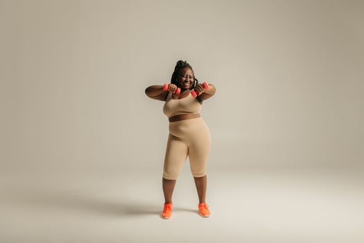 Full length happy plus size African woman in sportswear exercising with dumbbells on studio background photo