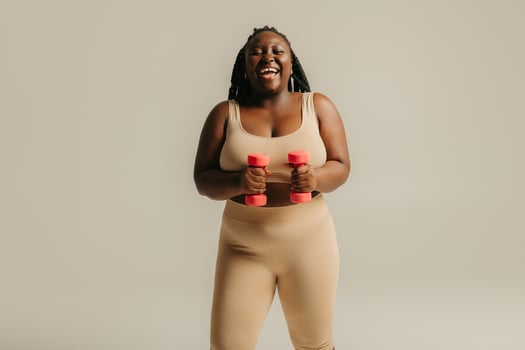 Happy plus size African woman in sportswear exercising with dumbbells on studio background photo