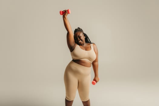 Confident plus size African woman in sportswear exercising with dumbbells on studio background photo