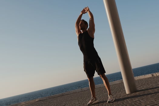 Active young man in sports clothing doing morning exercises with the sea on background photo
