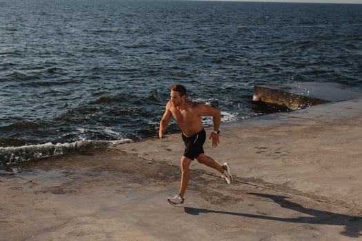 Top view of confident athletic man jogging by the pier with the sea on background photo